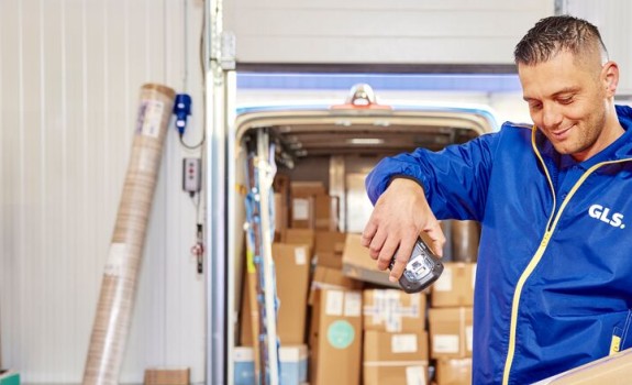 Man in GLS uniform scanning box in front of van filled with parcels